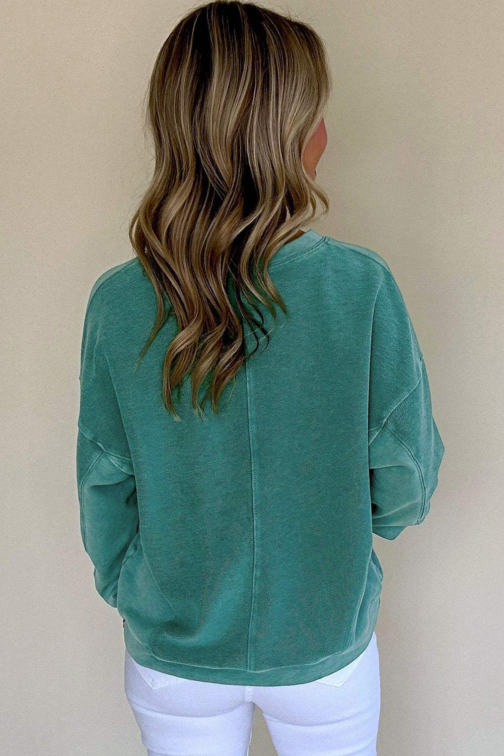 Person wearing a teal sweatshirt against a beige background