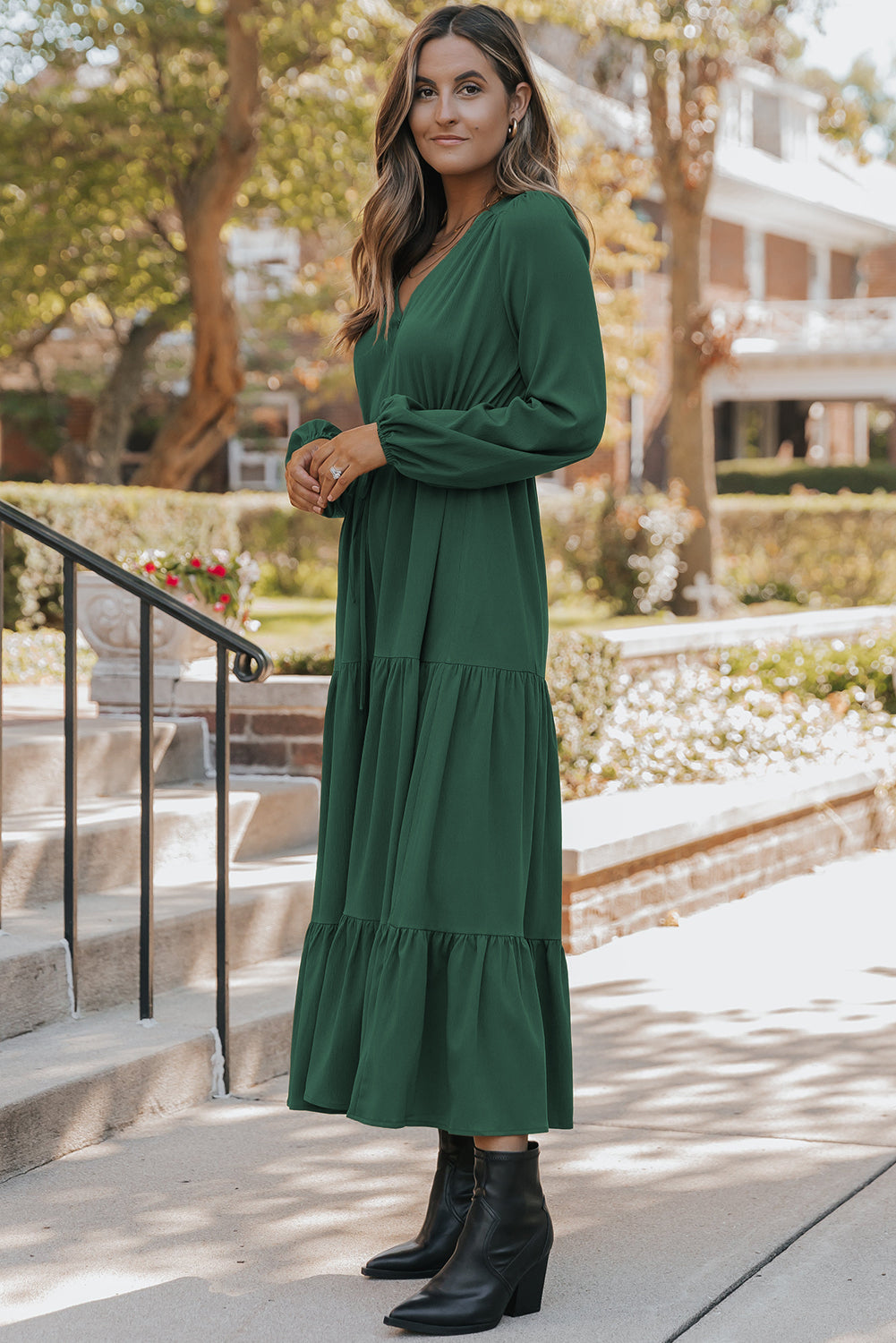 Woman wearing a green dress with long sleeves and ruffled layers, standing outdoors.