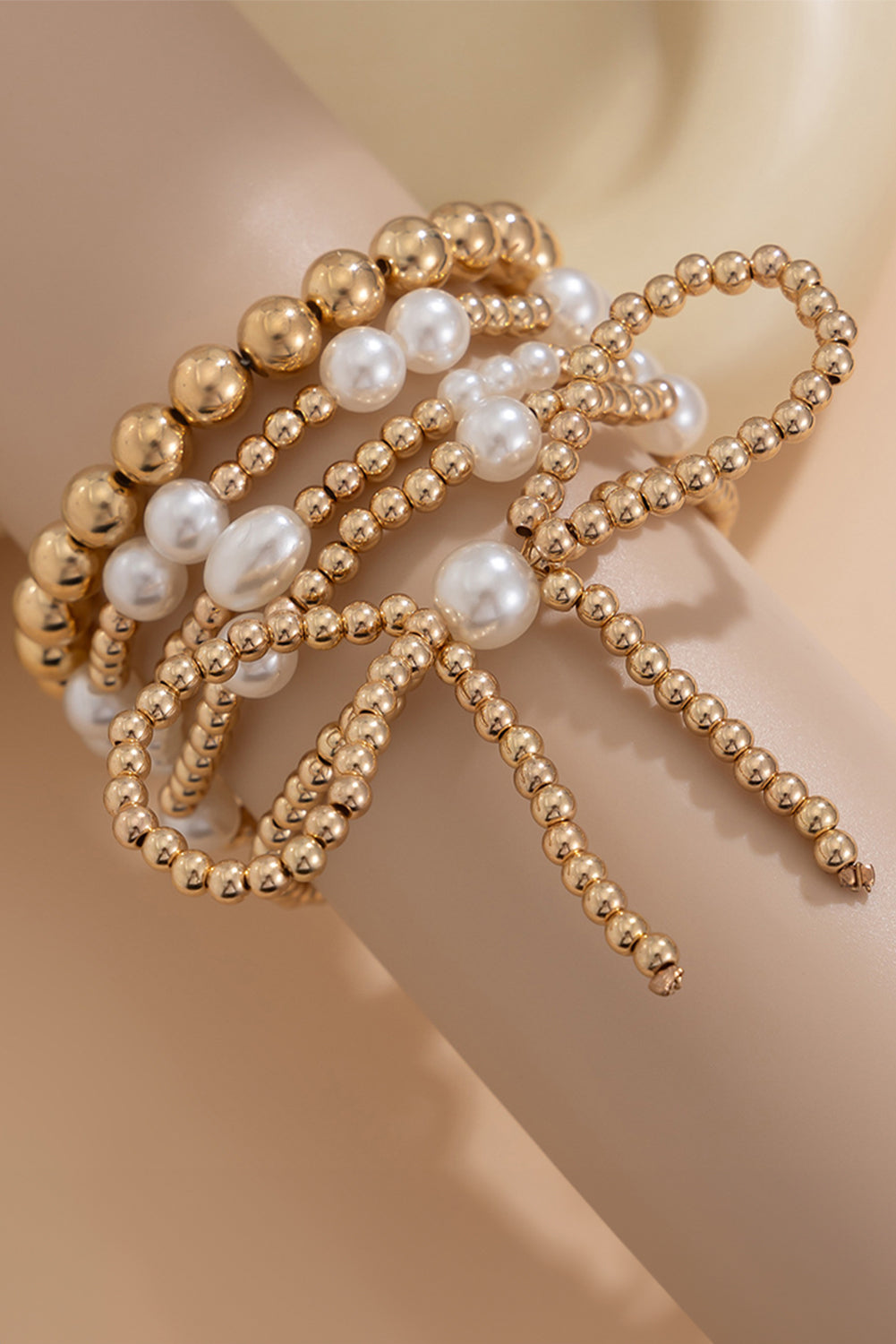 Gold and pearl beaded bracelet on a mannequin arm against a beige background