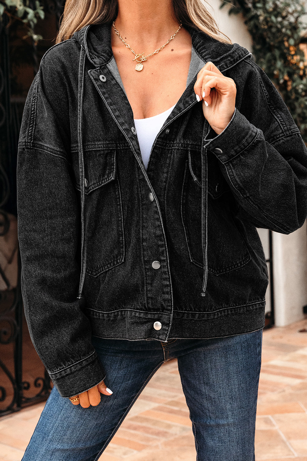 Person wearing a black denim jacket and blue jeans outdoors.
