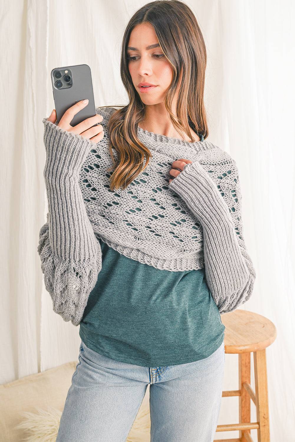 Woman wearing a gray oversized sweater over a green shirt, taking a selfie.