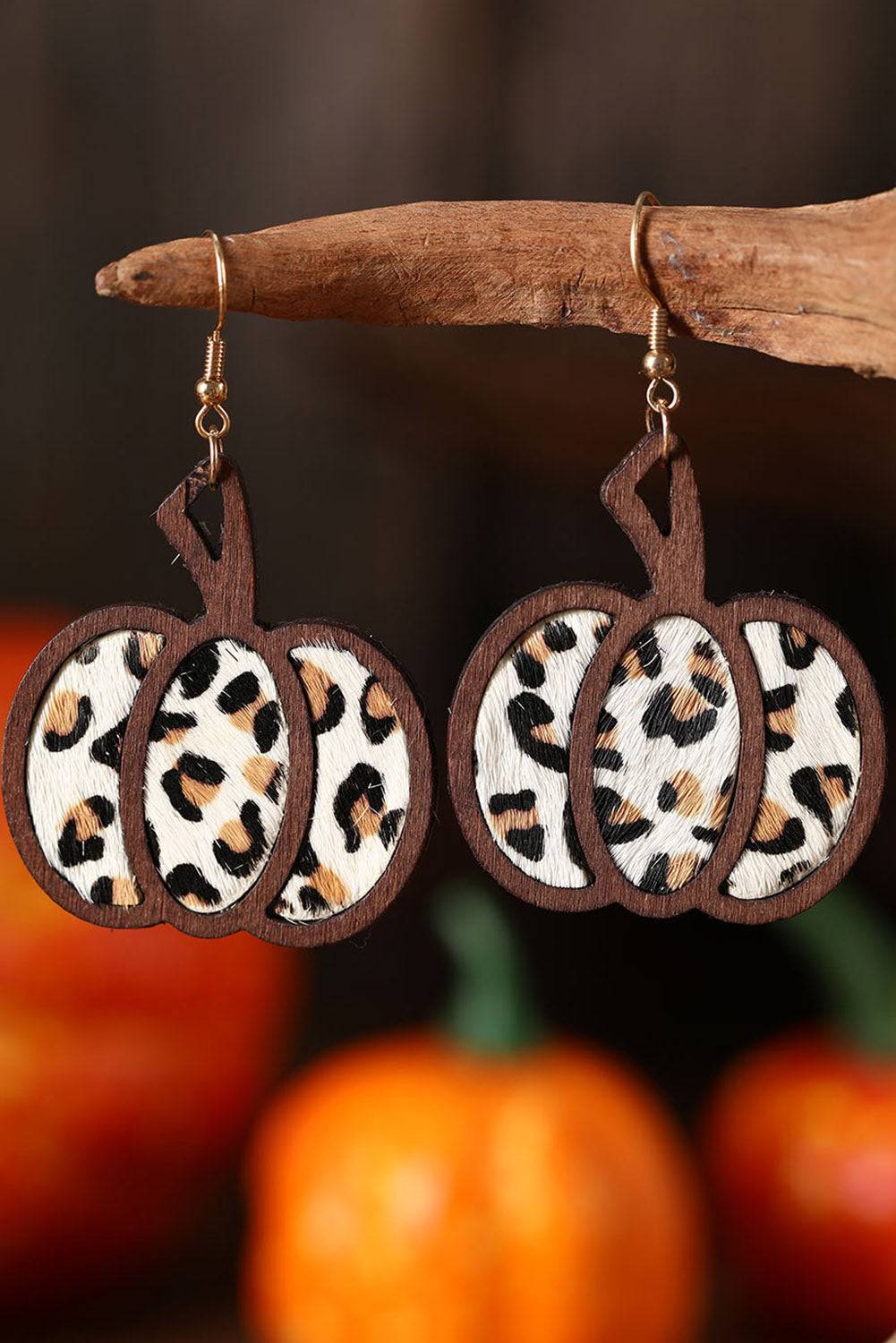 Leopard print pumpkin earrings hanging on a branch with pumpkins in the background.