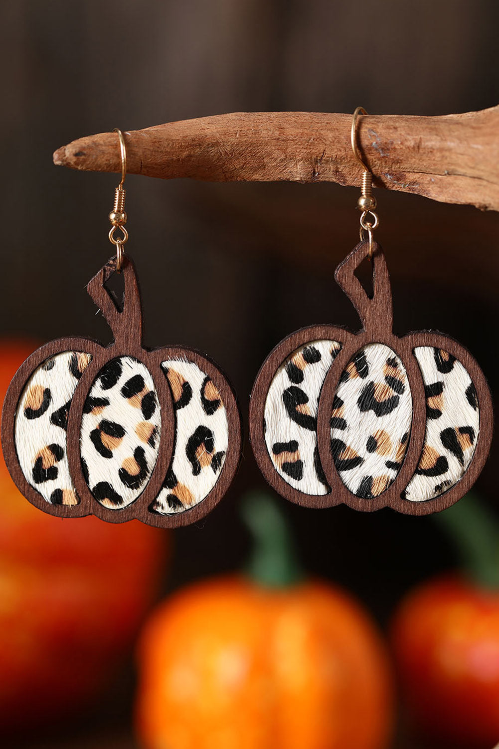 Leopard print pumpkin earrings hanging on a branch with pumpkins in the background.