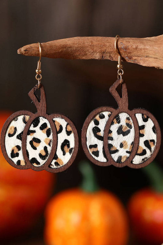 Leopard print pumpkin earrings hanging on a branch with pumpkins in the background.