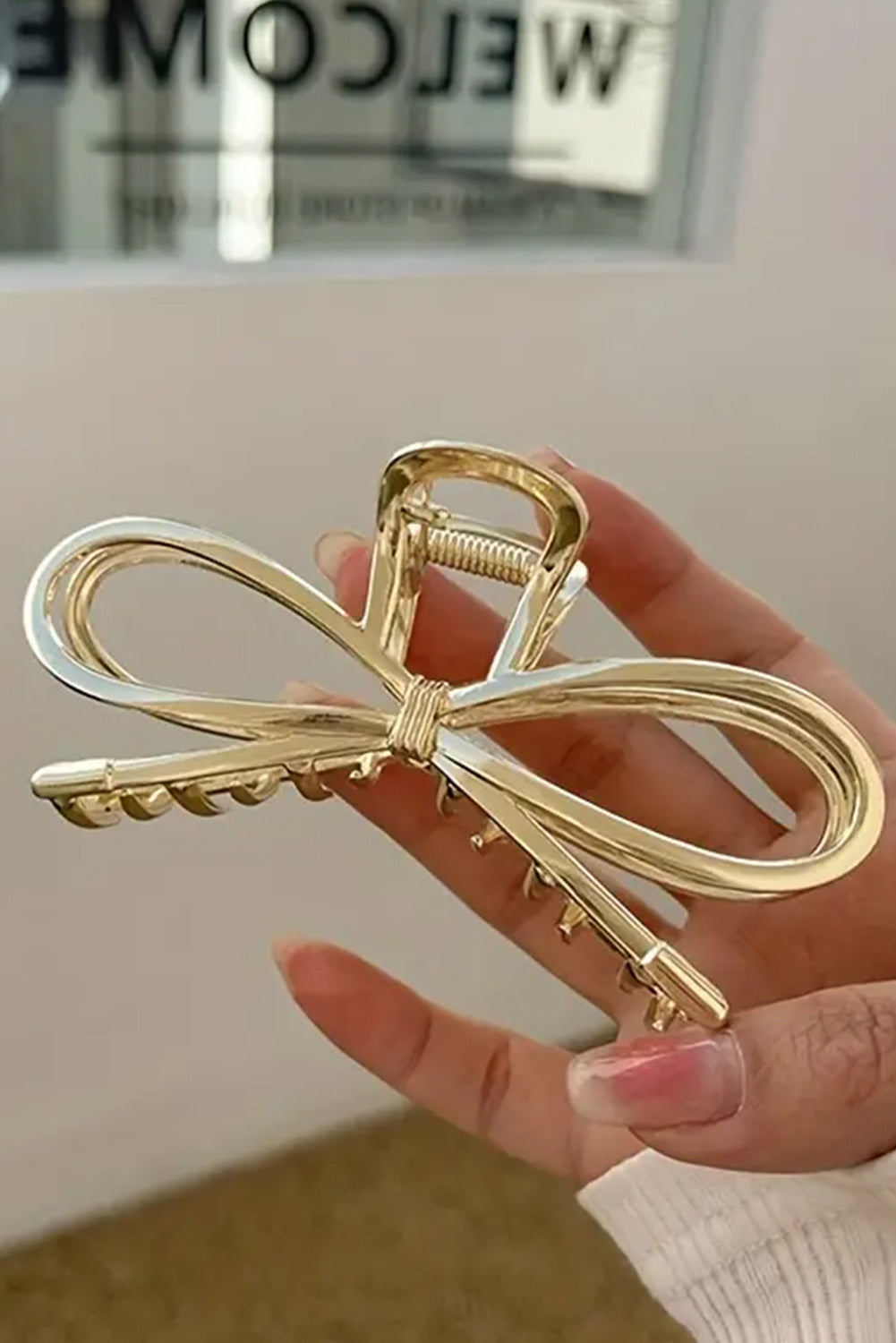 Gold bow-shaped hair clip held by a hand against a neutral background