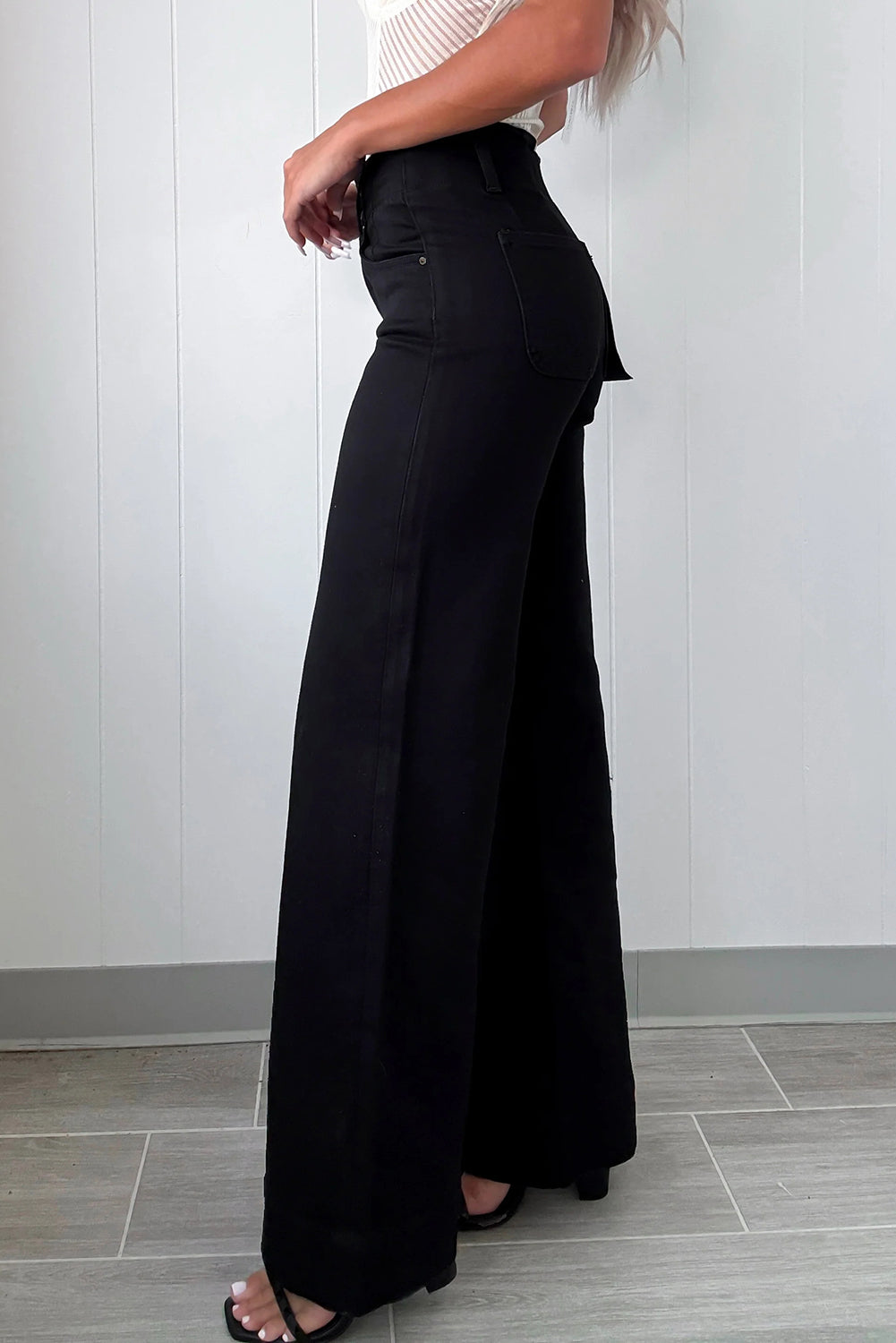 Person wearing black wide-leg pants against a white wall.