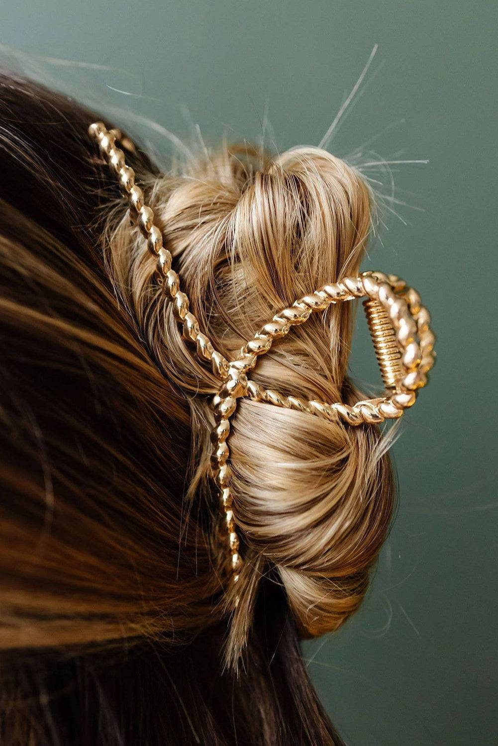 Gold hair accessory in a styled bun against a green background