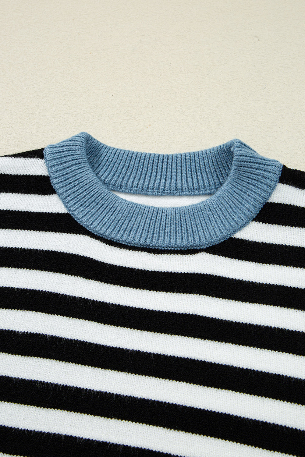 Close-up of a black and white striped sweater with a blue ribbed collar on a beige background