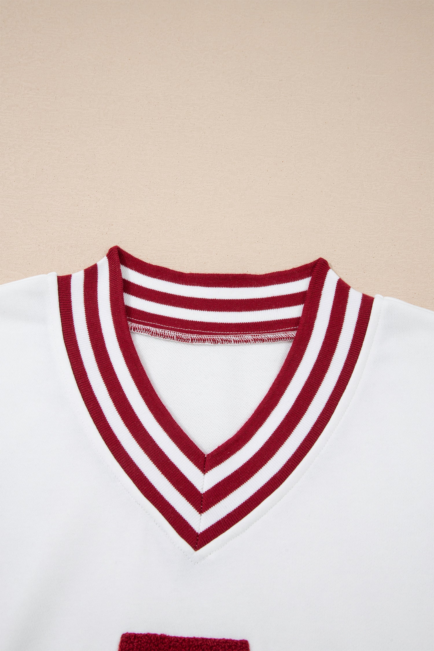 Close-up of a white shirt with red V-neck collar on a beige background