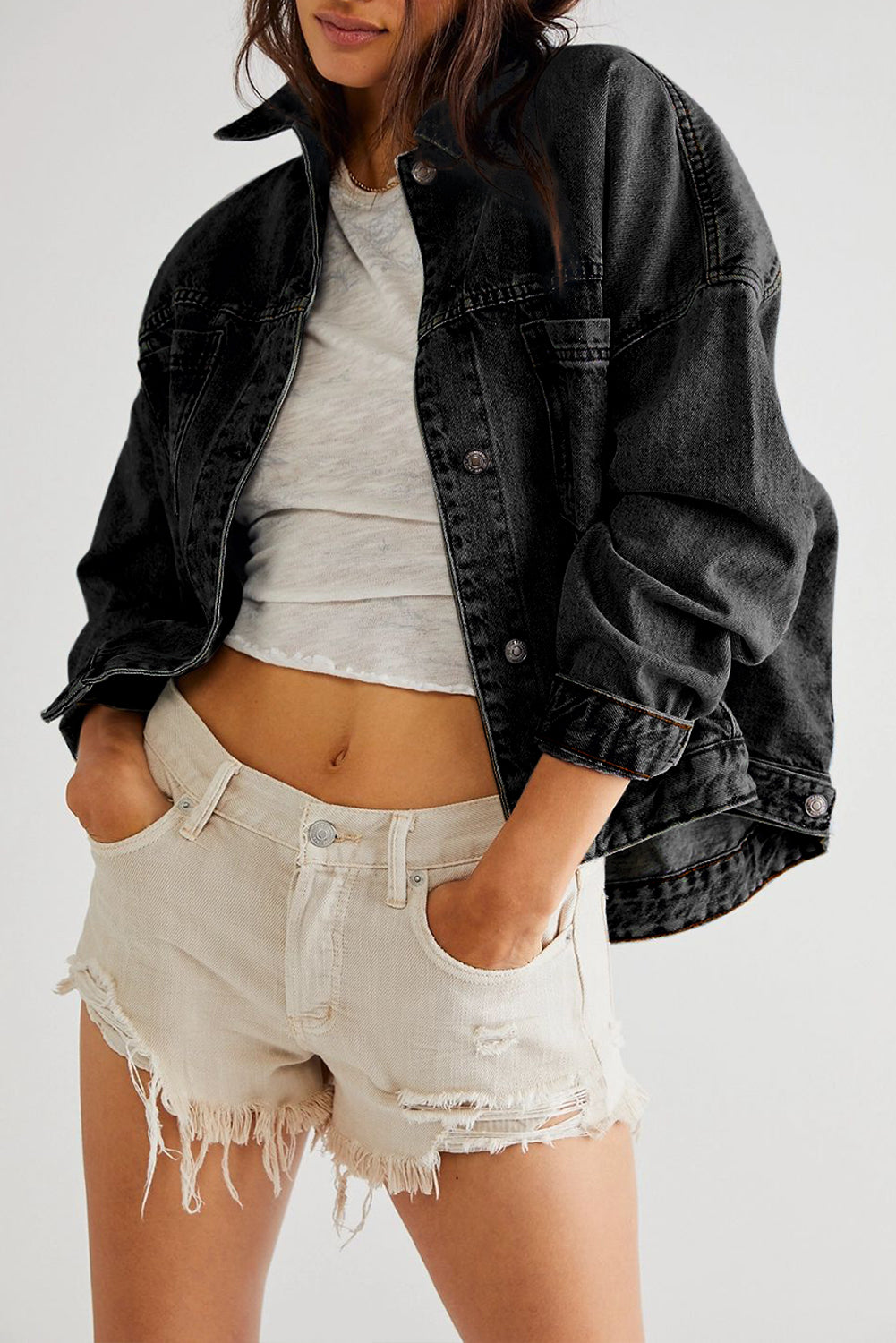 Person wearing a black denim jacket, gray crop top, and beige shorts on a white background