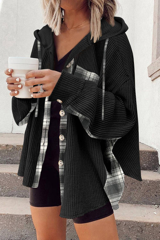 Person wearing a black cardigan over a plaid shirt, holding a white cup.