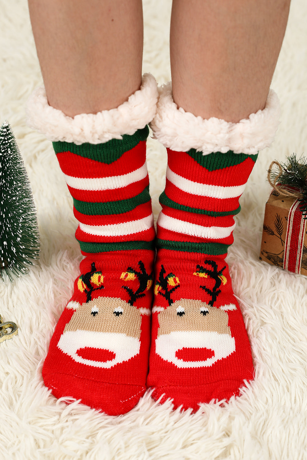 Red and green striped socks with reindeer faces on a fluffy white surface.