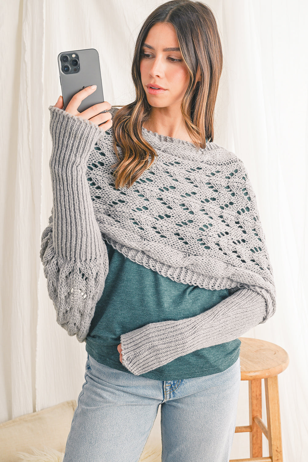 Woman wearing a gray knit shawl over a green sweater indoors.