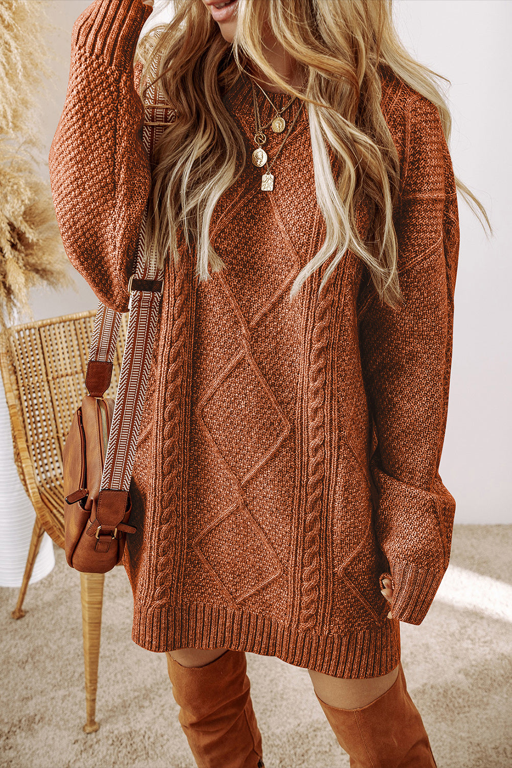 Person wearing a brown cable knit sweater dress with knee-high brown boots indoors.