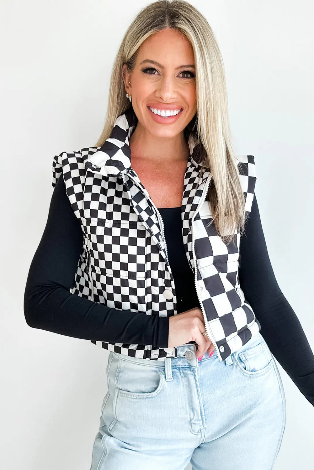 Woman wearing a checkered vest over a black long-sleeve shirt with light blue jeans on a white background