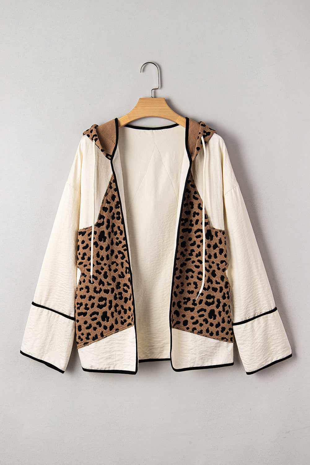 Leopard print jacket with cream and black accents on a wooden hanger against a gray background