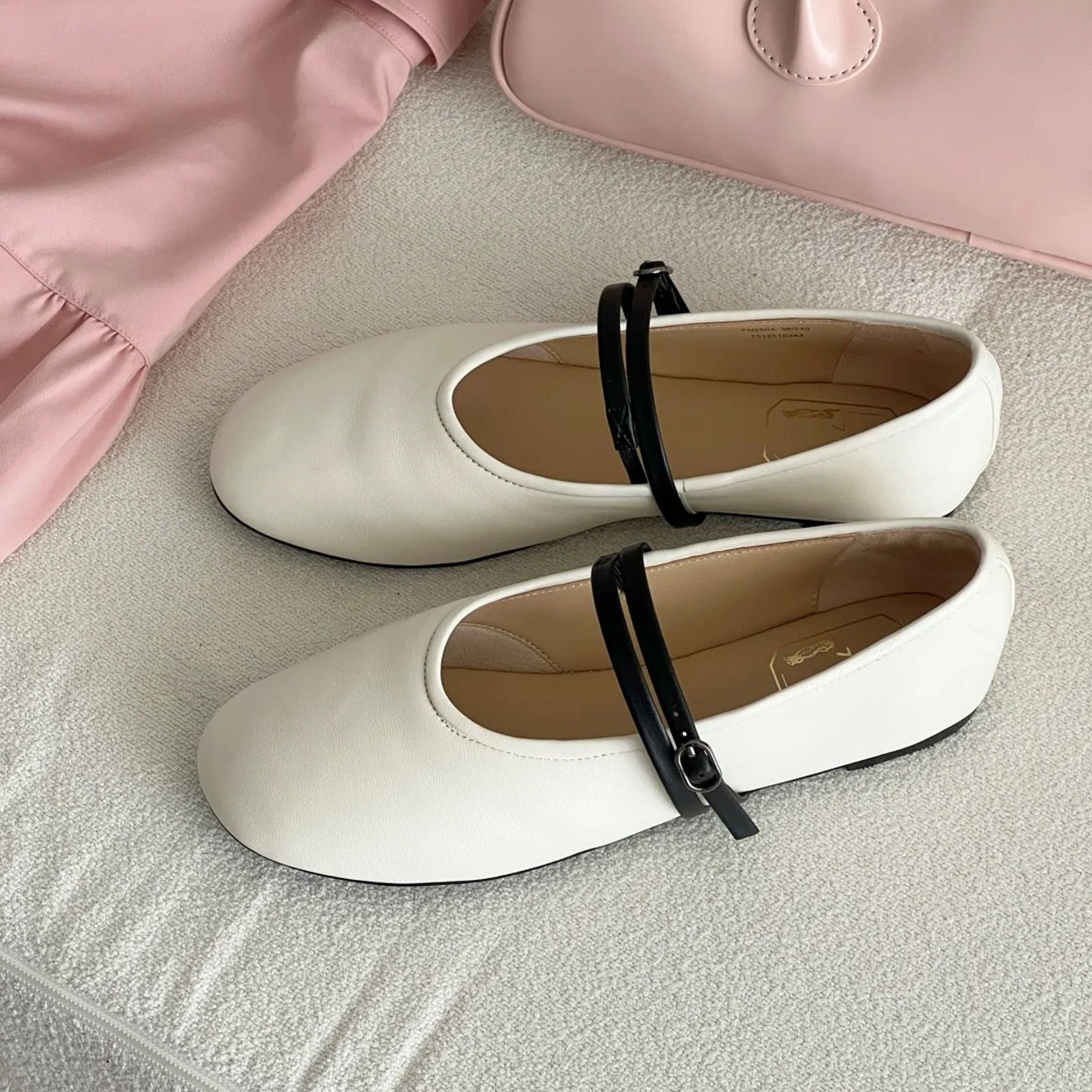 White shoes with black straps on a textured surface with a pink garment in the background