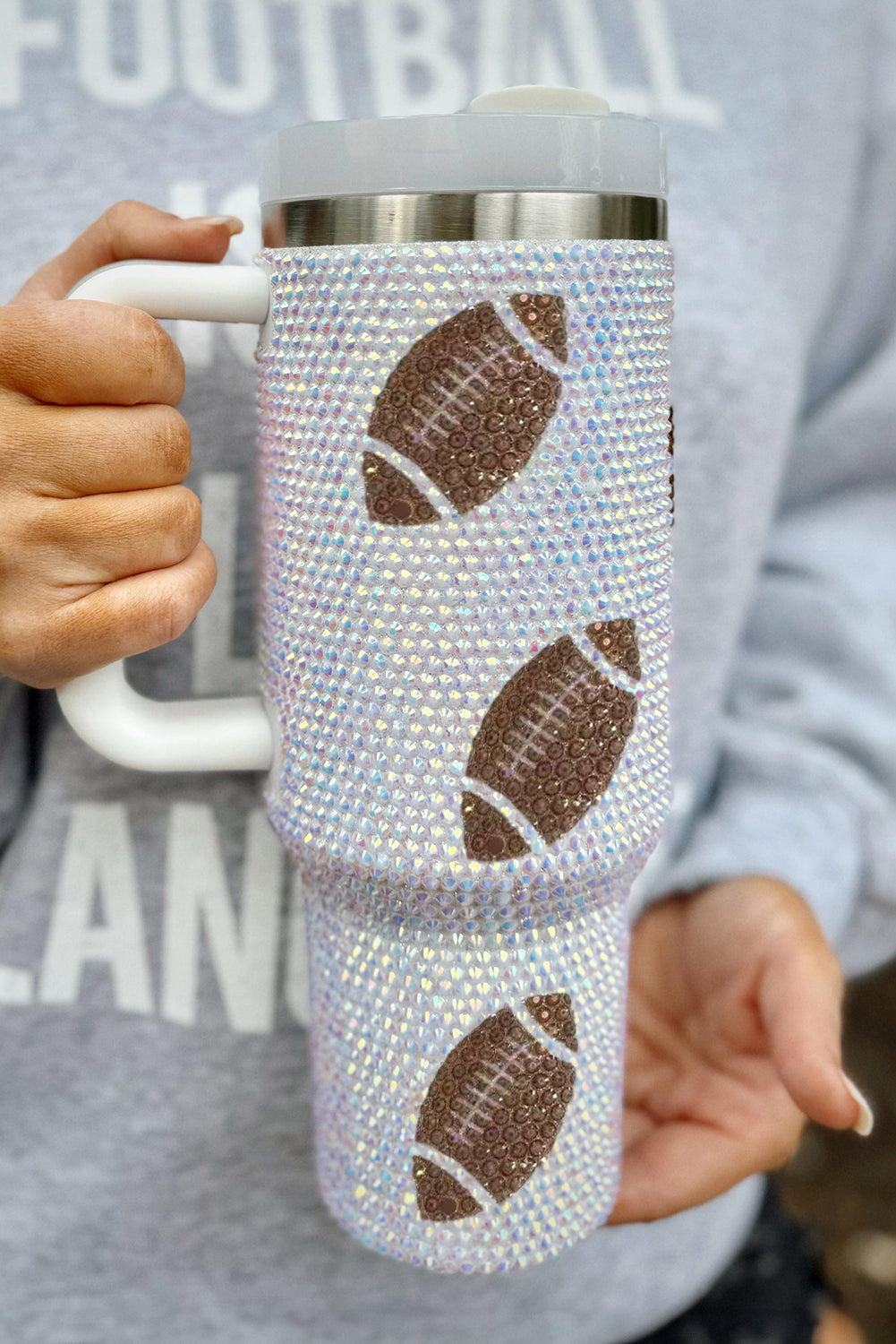 Person holding a blinged-out tumbler with football designs