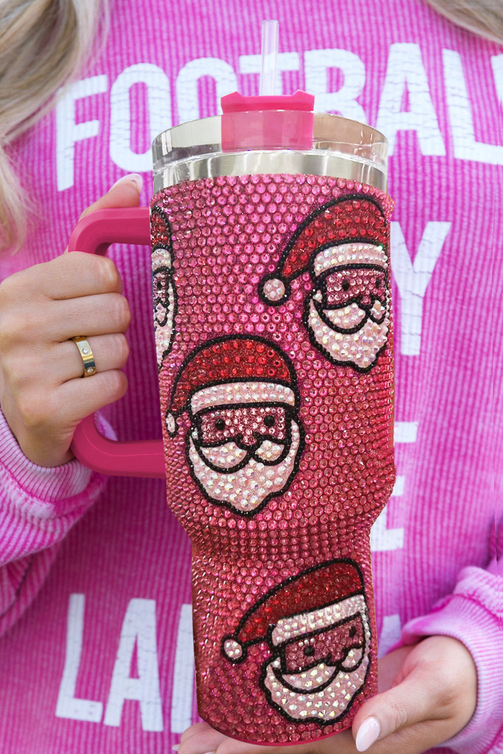Pink tumbler with Santa face designs held by a person wearing a pink sweatshirt.