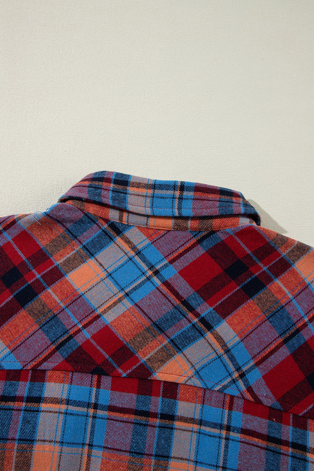 Close-up of a plaid shirt with red, blue, and orange patterns on a light background