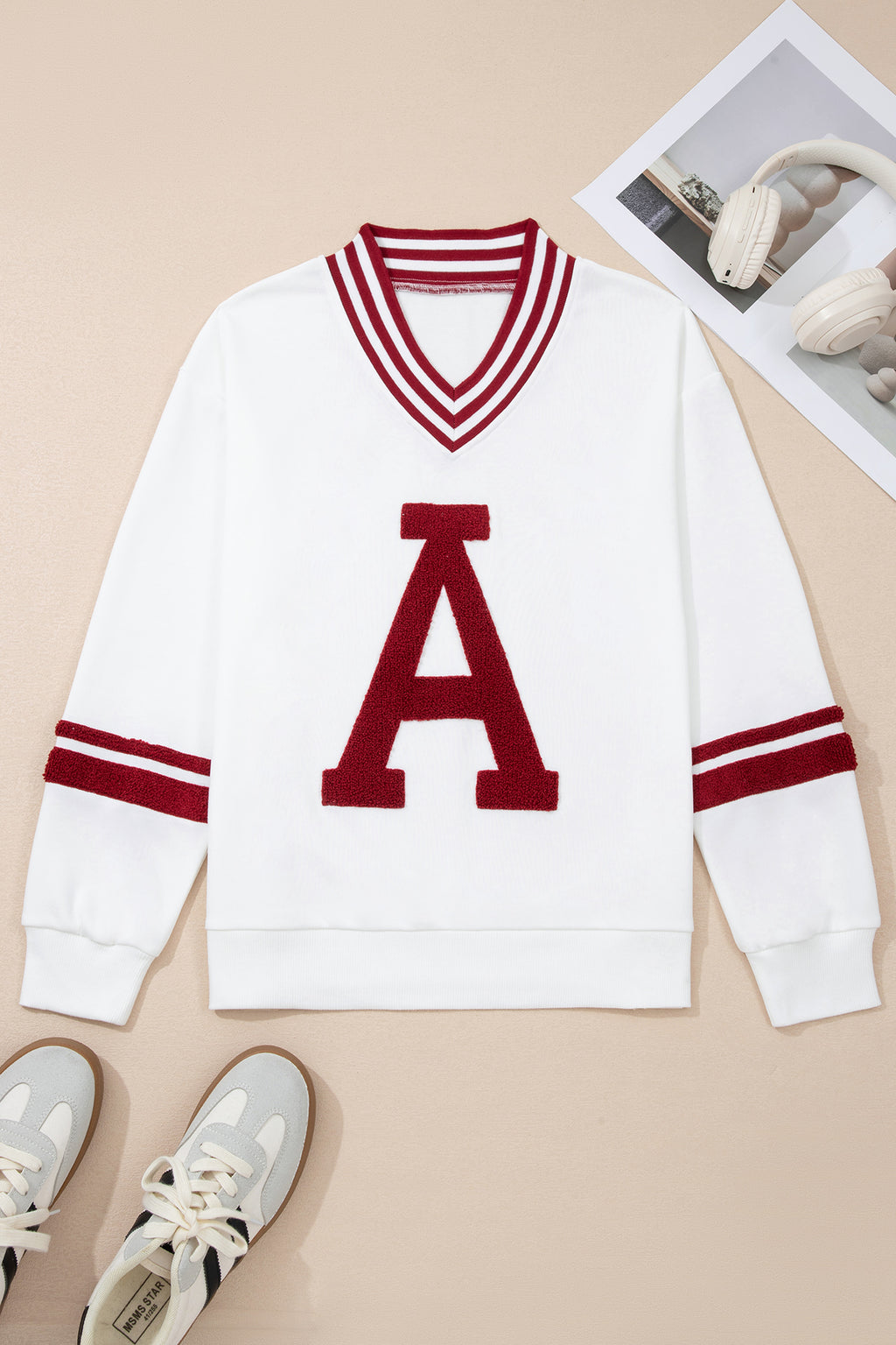 White sweater with red letter 'A' and stripes on a beige background