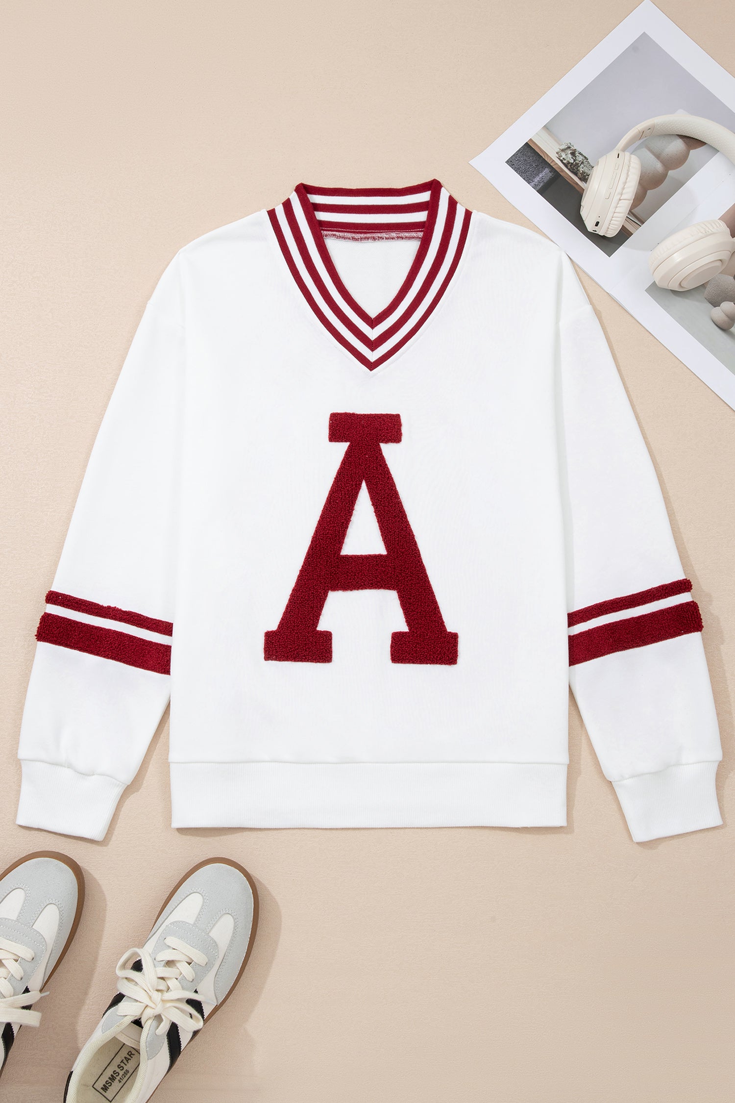 White sweater with red letter 'A' and stripes on a beige background