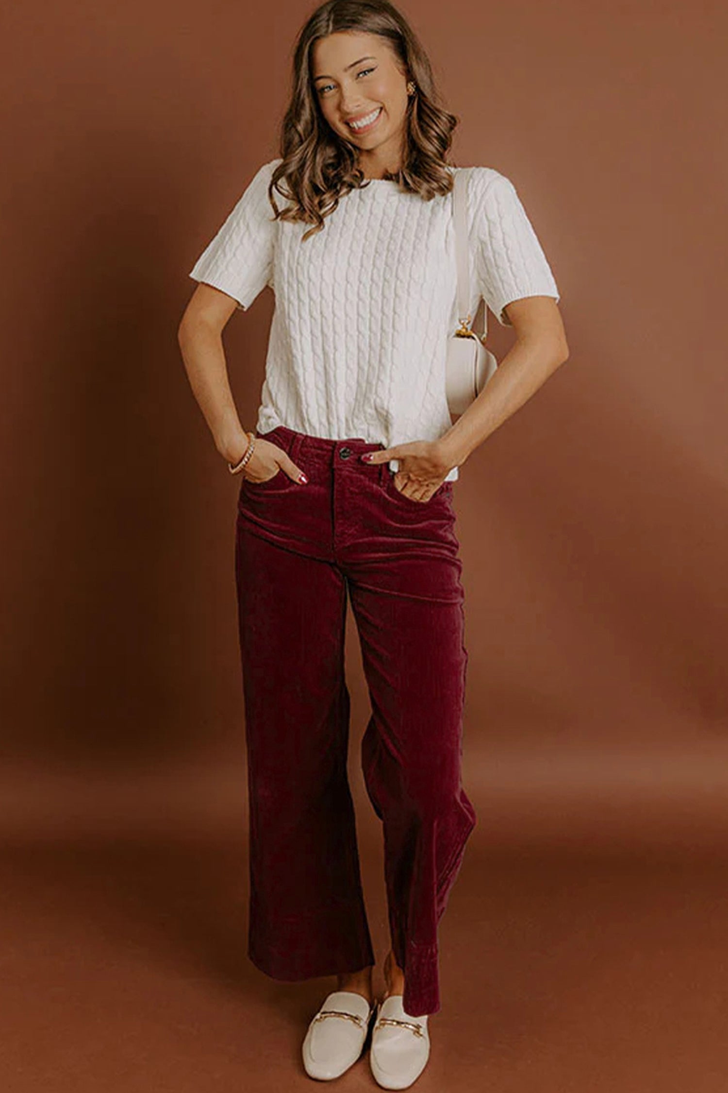 Woman wearing a white top and burgundy pants against a brown background