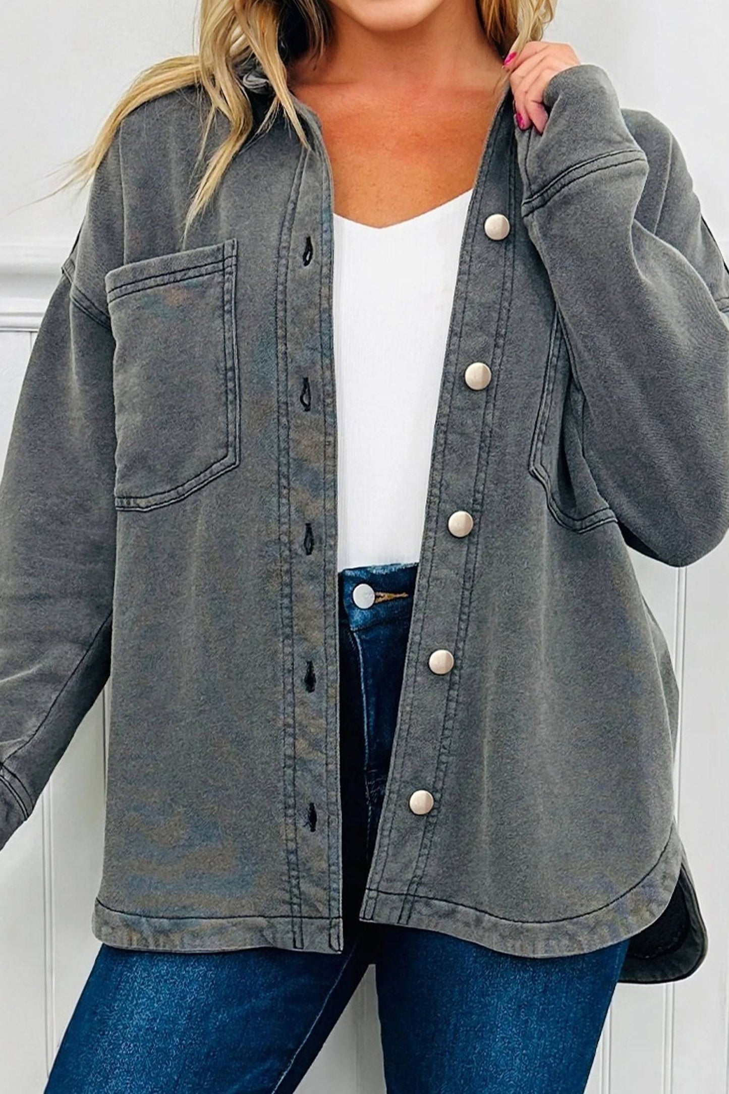 Person wearing a gray button-up jacket over a white shirt and blue jeans against a white background