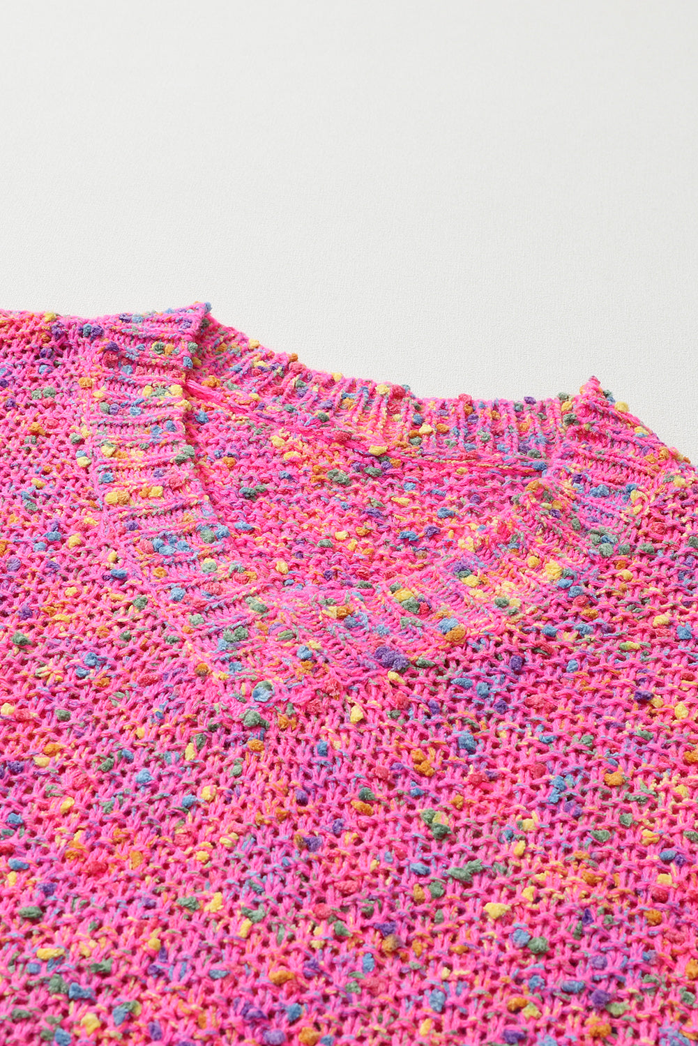 Close-up of a pink textured fabric with colorful speckles on a light gray background
